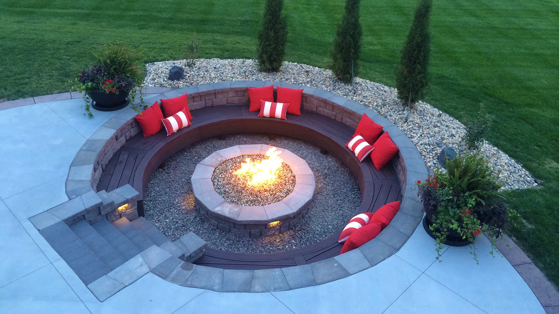 A round stone firepit surrounded by a seating area detailed with red pillows in Omaha, NE. 