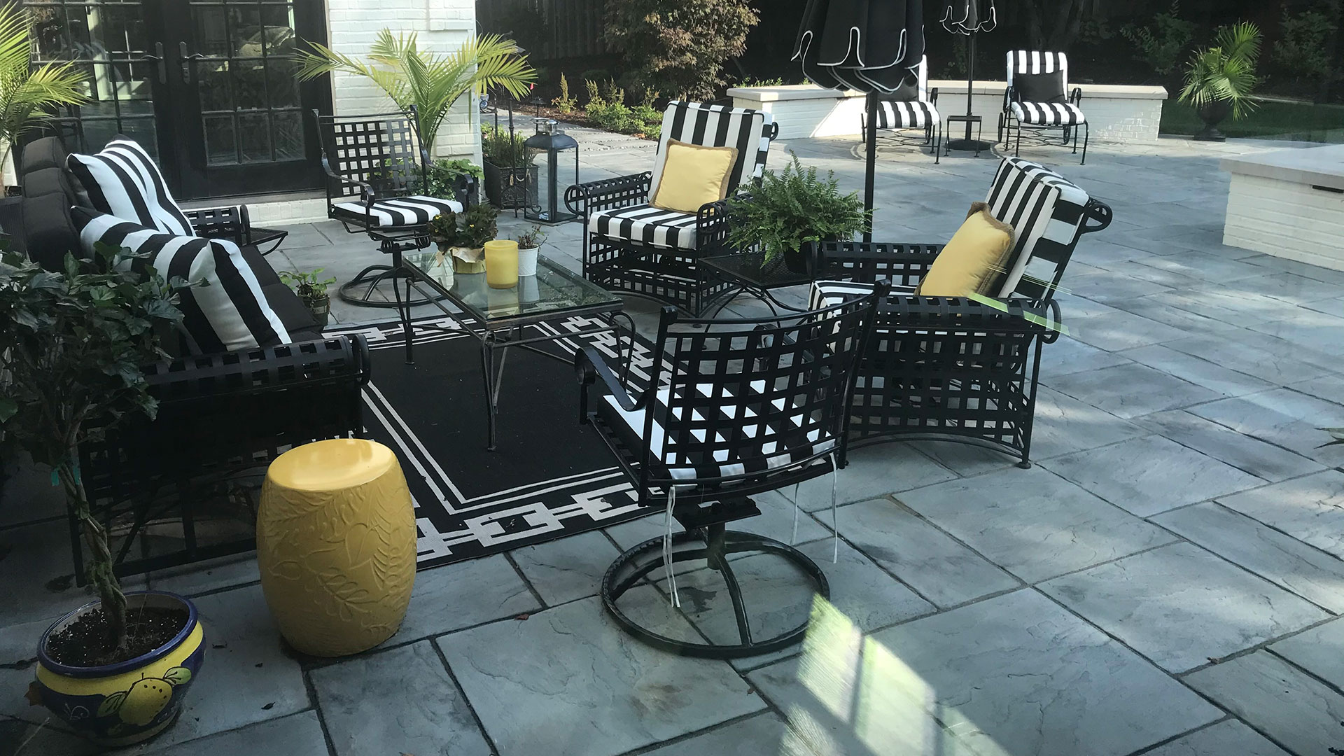 A grey flagstone patio with black, white, and yellow furniture installed behind a home in Chalco, NE. 