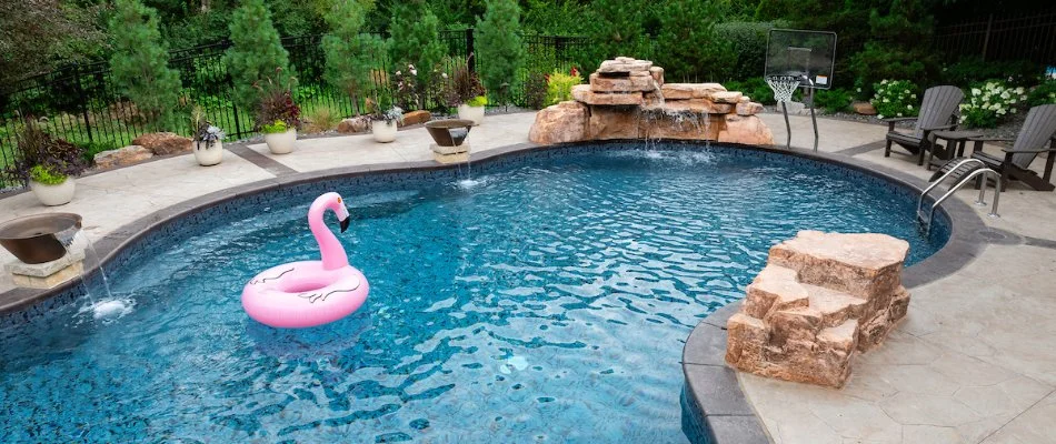 Pool with a rock water feature, basketball hoop, and pick flamingo float in Omaha, NE.