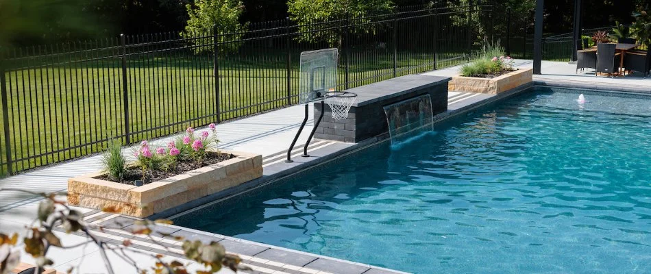 A pool in Elkhorn, NE, with a waterwall, basketball net, and planters.