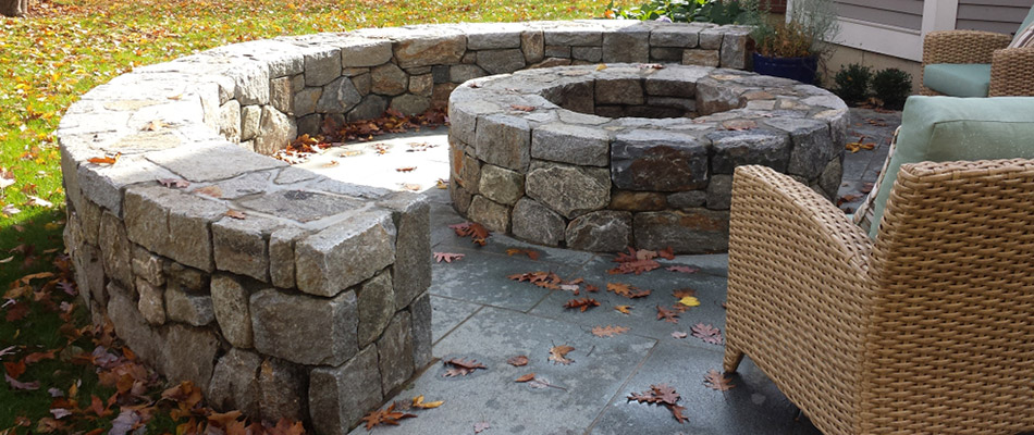 A stone seating wall surrounding a round fire pit behind a home in Blair, NE. 