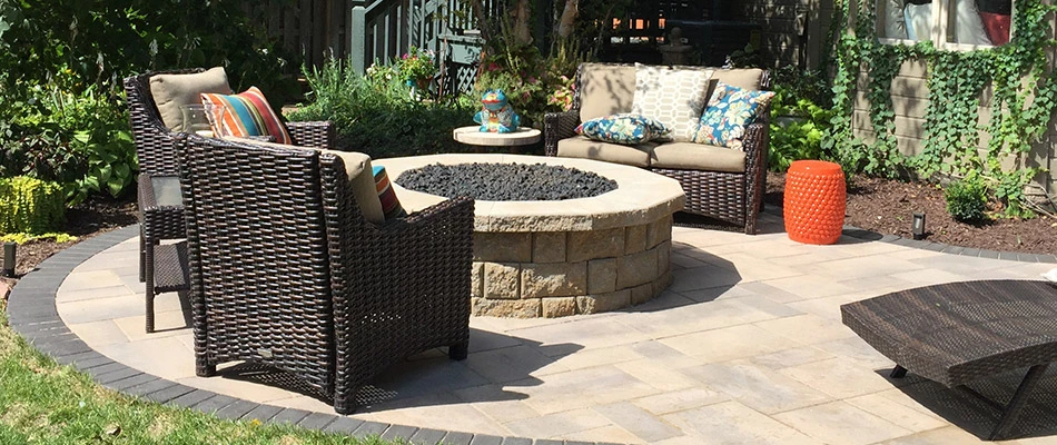A stone fire pit surrounded by wicker chairs and colorful pillows in an Ashland, NE backyard. 